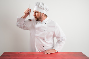 Young male chef in white uniform holding cooking ladle