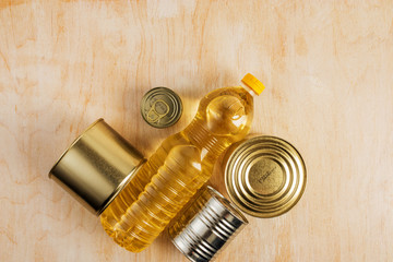 a bottle of sunflower oil and metal cans of various canned food on a light wooden background