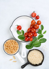 Food background with vine tomatoes, spinach leaves, white rice, fusilli pasta and cast iron skillet. Top view, banner, copy sapce. Vegan or diet food concept. Composition with ingredients for cooking.