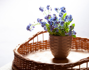 Fototapeta na wymiar Bouquet of blue forget-me-not flowers on wicker table on white