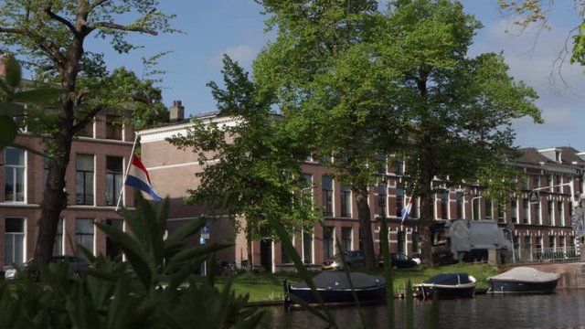 Slide shot of garbage truck driving past Dutch flag flying at half mast on a house along a canal