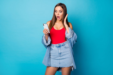 Portrait of astonished girl student use smart phone impressed by social network information scream wow omg wear good look jeans singlet isolated over blue color background
