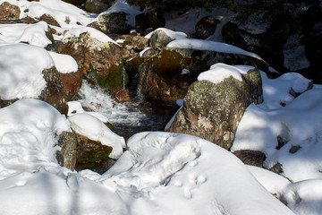 A mountain stream flows between the snowy rocks