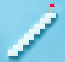 Concept to achieve the goal, the upward movement. White staircase with a red flag on the top step...