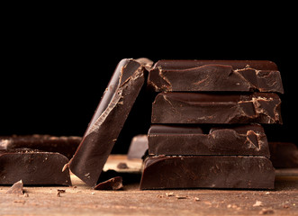 broken black chocolate on a wooden table, culinary sweet ingredient