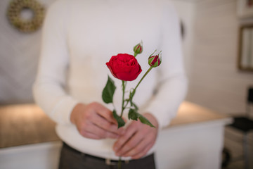 Man in white sweater holding vase with peonies inside the room