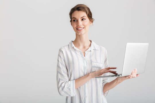Image of joyful beautiful woman smiling and typing on laptop