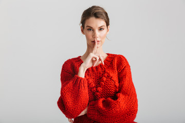 Image of young pretty woman in red sweater showing silence gesture