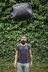 brutal bearded man courier in shorts and a t-shirt is holding a large gray bag. the courier is holding a huge parcel.