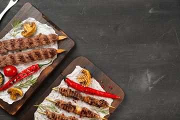 Grilled Lula kebab on skewers served on wooden board, black table background