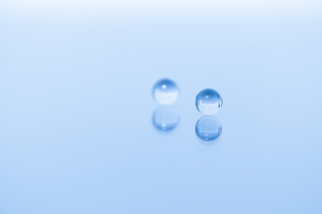 Abstract composition, two marbles are mirrored on a shiny surface, the centre marble is blurred, treating the colours monochromatic blue.