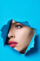 Beautiful woman with pink lips looking across ripped blue paper