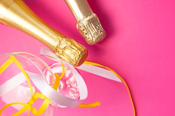 Two champagne wine bottle neck in gold silver foil,near champagne glass and colored satin ribbons on bright pink, flat lay top view. Concept of celebrating, birthday, congratulations, happiness, party
