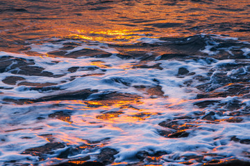 Beautiful waves with foam, illuminated by the setting sun on the sea. Texture of the sea surface with ripples at sunset.