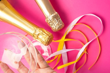 Two champagne wine bottle neck in gold silver foil,near champagne glass and colored satin ribbons on bright pink, flat lay top view. Concept of celebrating, birthday, congratulations, happiness, party