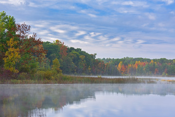 Foggy autumn landscape of the shoreline of Deep Lake with unique clouds and with mirrored reflections in calm water, Yankee Springs State Park, Michigan, USA