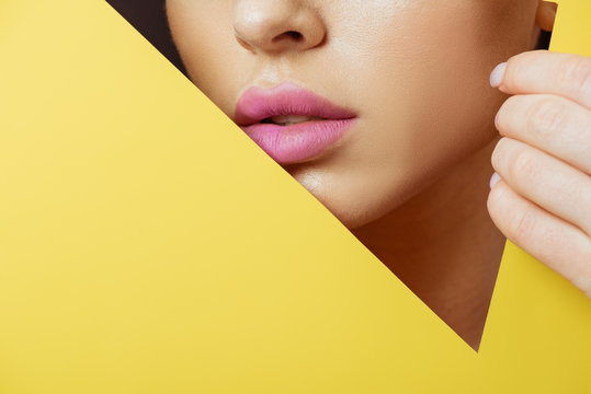 Fototapeta Cropped view of woman with pink lips in triangular hole touching yellow paper on black