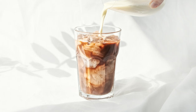 Milk cream is poured into a iced coffee cold brew.  Coffee cold drink with ice and milk.