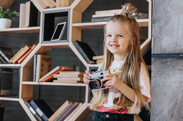 Little girl with a camera in hands on a background of books