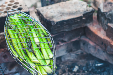 A barbecue net with green asparagus is cooked on smoke at a stake.