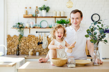 A small child girl is playing in the bright Scandinavian-style kitchen at the table. Father and daughter play with grits. The concept of Montessori education. Eco kitchen.