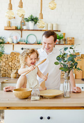 A small child girl is playing in the bright Scandinavian-style kitchen at the table. Father and daughter play with grits. The concept of Montessori education. Eco kitchen.