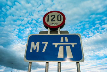 Looking up at M7 motorway sign, 120km per hour speed limit sign in Ireland,