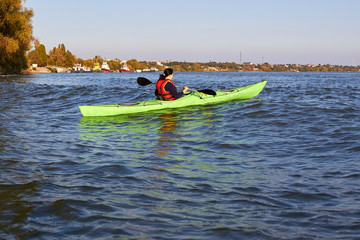 Woman rowing on green kayak on a Danube river near shore