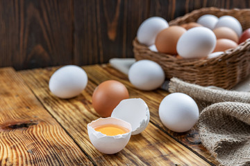 Farm eggs white and brown lie on a wooden table and in a basket, close-up, low light, selective focus, shallow depth of field. Organic food concept
