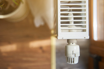 Radiator in the apartment. White heated battery. Thermostat head of a heating radiator in an apartment, office.