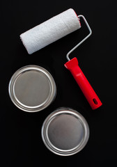 Paint roller and two cans of paint on a black background. View from above. Vertical