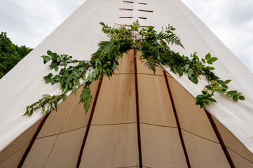 Close up of the summer wedding tipi in a field. Tee pee built on green grass. Traditional teepee tent wigwam located in nature. Natural decoration for wedding.