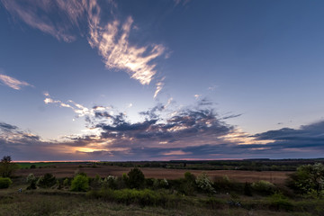 Obraz premium Blue red sky background with evening fluffy curly rolling clouds with setting sun. Good windy weather
