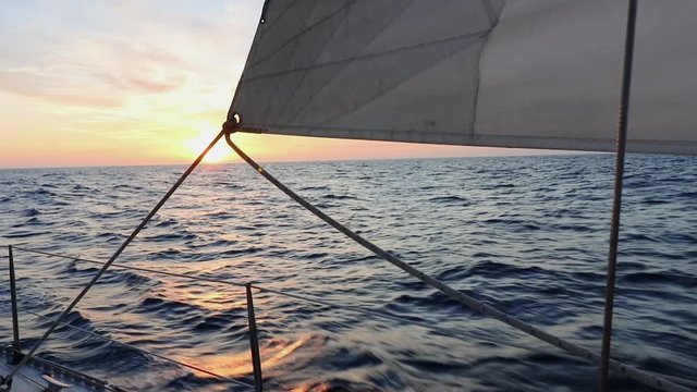 A small sailboat goes sailing at sunset at the sea