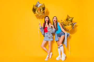 Full length body size view of nice attractive cool fashionable cheerful cheery girls holding in hands air balls having fun isolated on bright vivid shine vibrant yellow color background