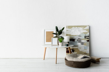 green plants, frames and lamp on white coffee table near painting and books in modern apartment