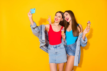 Positive two people youth sisters girls bloggers enjoy summer trip take selfie smartphone hold tasty yummy icecream make v-sign wear red blue singlet denim isolated bright shine color background