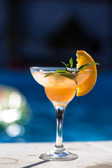 cocktail with orange, mint  and ice, blue pool background. Summer time and hot holiday