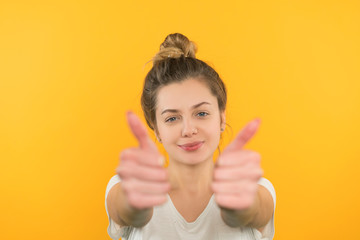 A young girl with blond hair on a yellow background, she is dressed in a white T-shirt and jeans,...