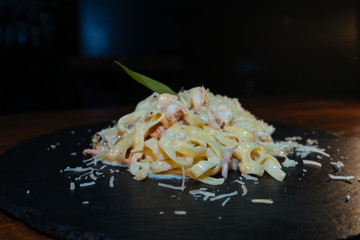 delicious Italian pasta with cheese, seafood, bacon, sausage on a black stone with Basil