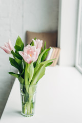 bouquet of pink tulip flowers in glass on windowsill with books