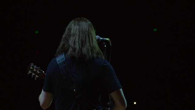 A man plays a guitar in front of the audience. Live concert of classic rock music. A musician in black clothes and long hair