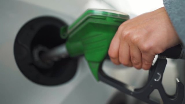 Woman fills petrol into her car at a gas station. Slow motion
