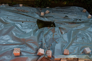Cobblestones weigh down a plastic sheet that is covering a paving construction site