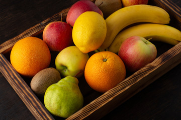 Set of fresh fruits in a wooden box on a dark background.