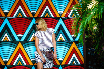 Fashionable beautiful blonde in dark glasses, standing against a bright wall with geometric patterns.The concept of recreation, tourism and travel.Summer holidays