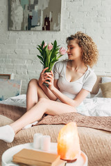 Obraz premium beautiful curly girl holding flowers in bedroom with Himalayan salt lamp