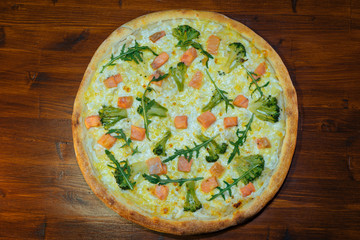 vegetarian Italian pizza with fish and cheese, broccoli and herbs on a wooden table
