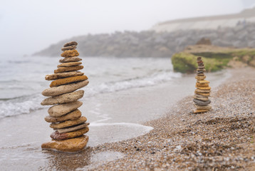 Fototapeta na wymiar Stones pyramid on sand symbolizing zen, harmony, balance. Ocean in the background. Soft focus.