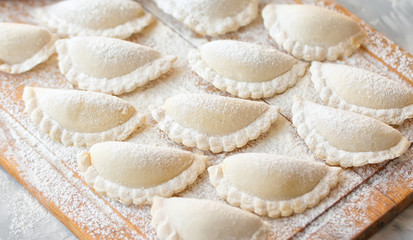 Raw dumplings on a wooden board on grey table.  The process of making dumplings. Close up.Top view